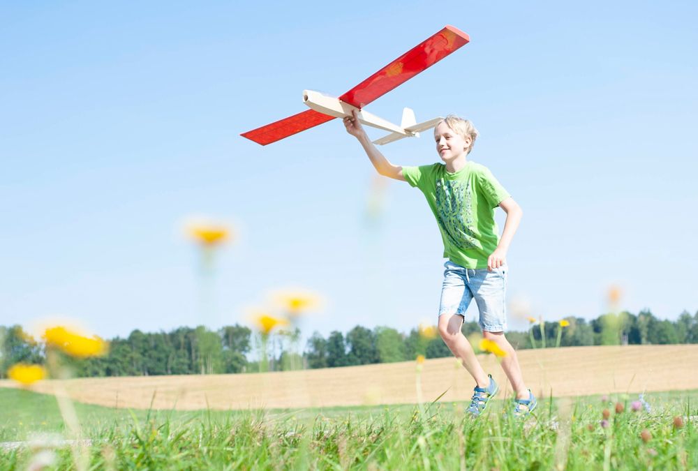 Foto Heuschnupfen, fröhlicher Junge rennt mit Modellflugzeug in der Hand auf einer Wiese