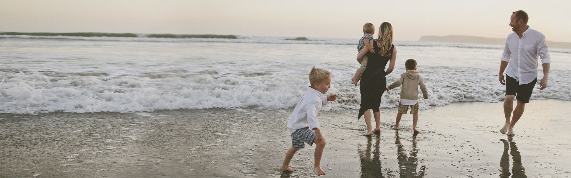 Teaser Atopie, glückliche Familie am Strand bei Sonnenuntergang